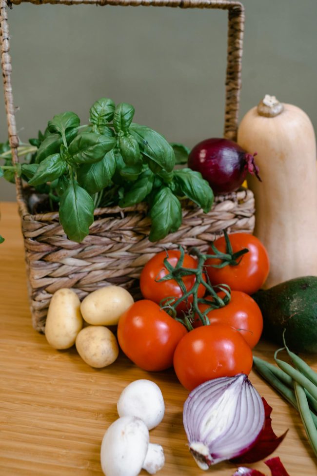 A vibrant collection of fresh organic vegetables displayed in a wicker basket on a wooden table.